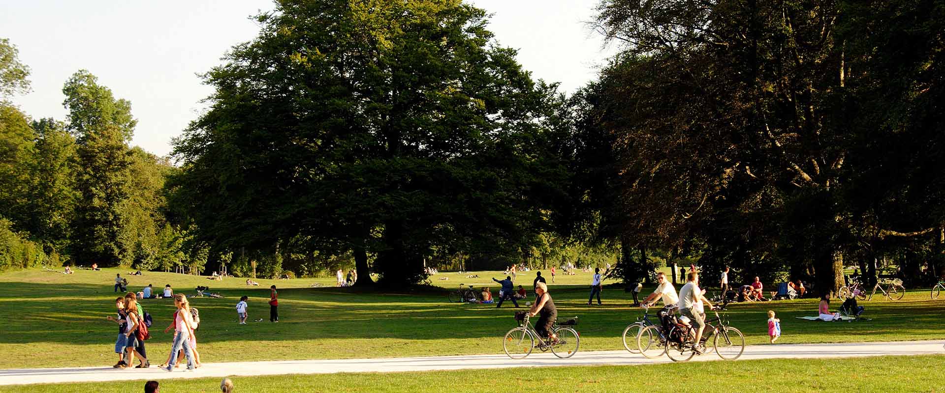 People strolling and cycling through a park on a sunny day.